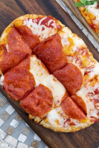 Pizza with pepperoni slices on a wooden serving board.