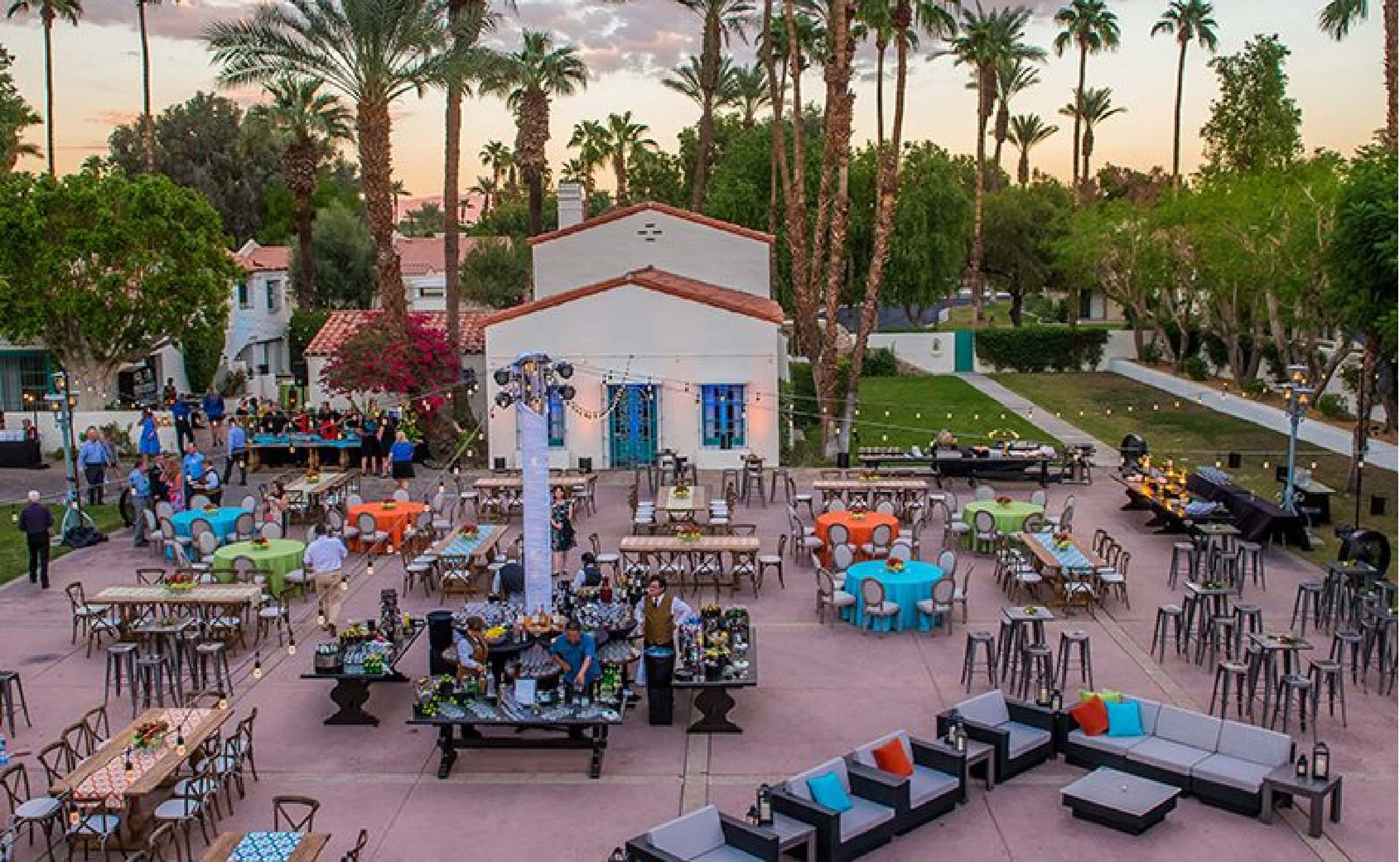 Outdoor wedding reception setup with elegant tables and chairs amid lush greenery and tall palm tree.