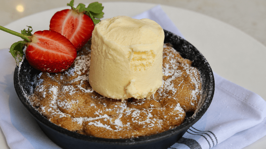 French toast with ice cream and strawberries on a black plate.