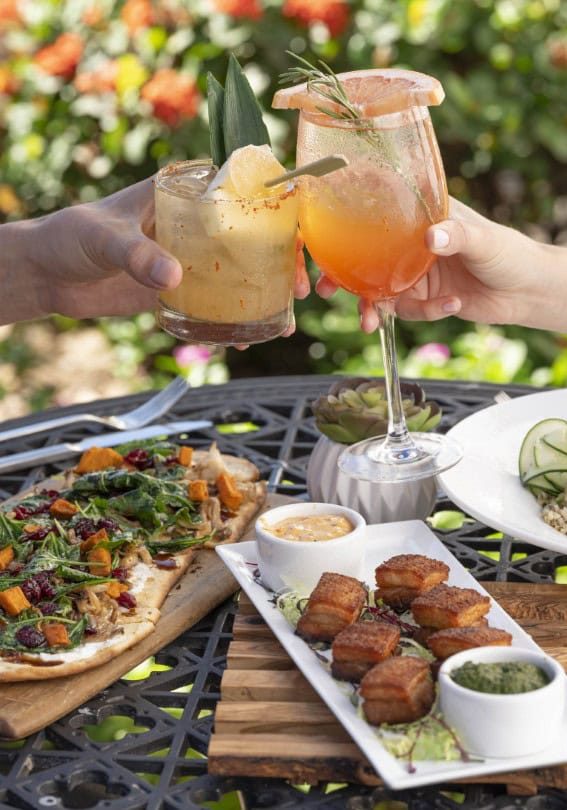 Two people clinking colorful cocktails outdoors.