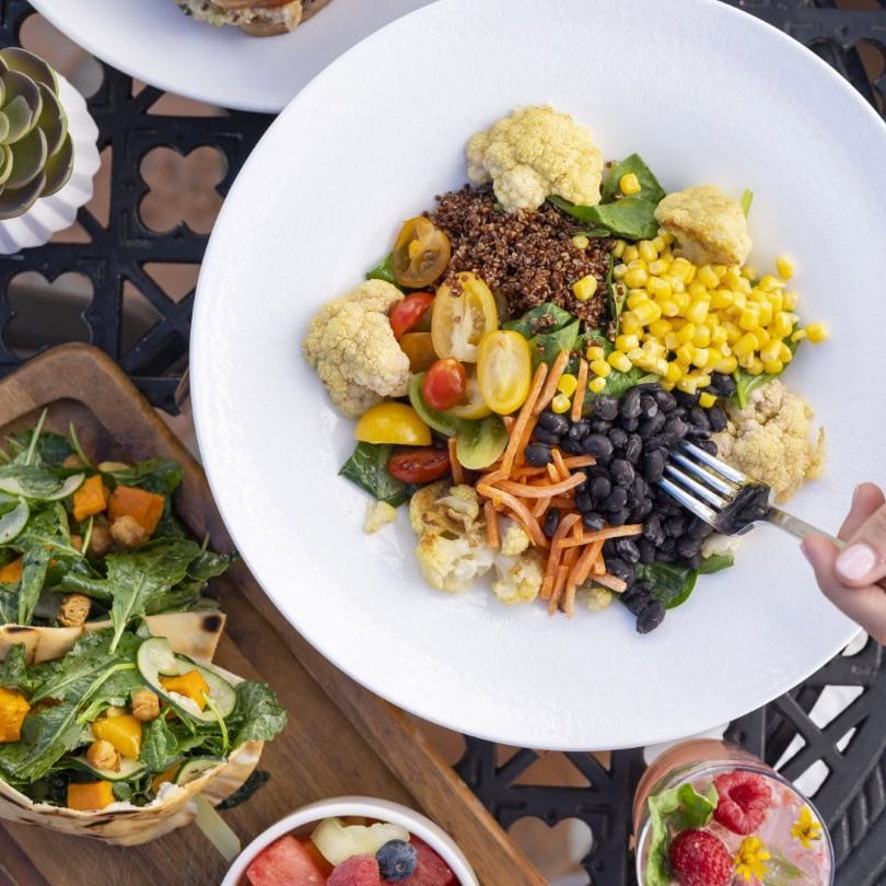 Vegetable salad with cauliflower, cherry tomatoes, corn, black beans, and greens on a white plate.