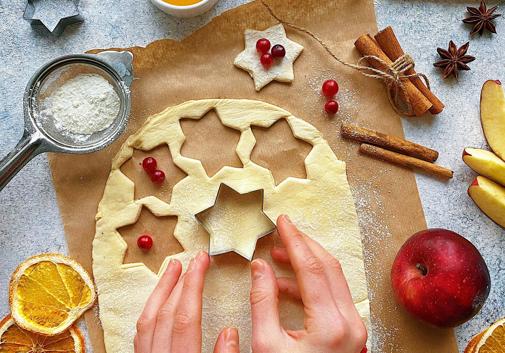Person cutting holiday star-shaped cookies with ingredients around.