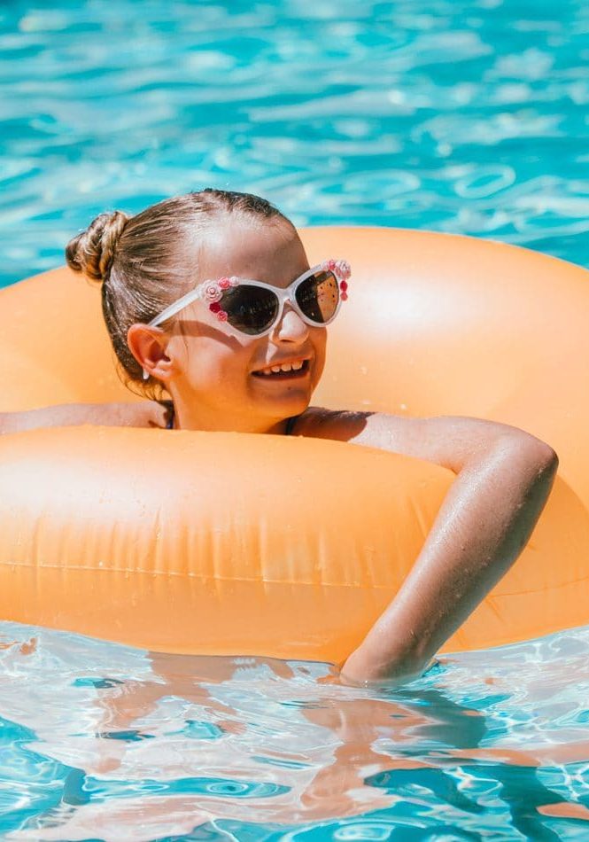 Child girl relaxing in pool on float ring, enjoying sunny weather.