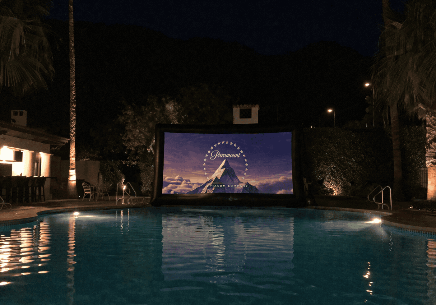 Night view of La Quinta Resort & Club pool with movie screen and palm trees.