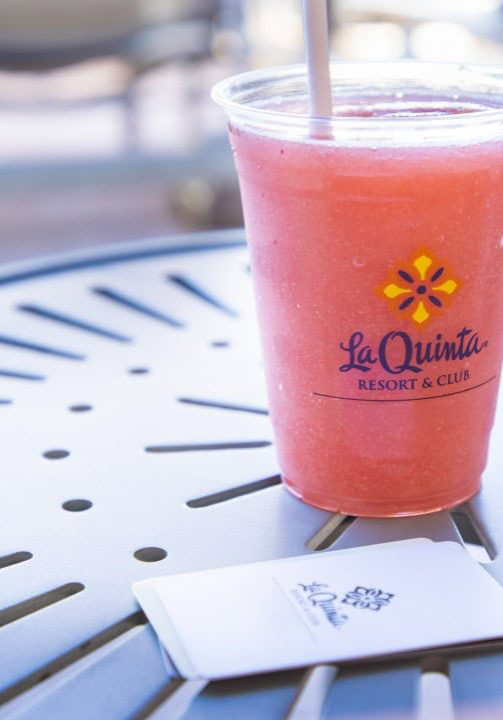 Pink smoothie in a clear cup with La Quinta logo on a table.