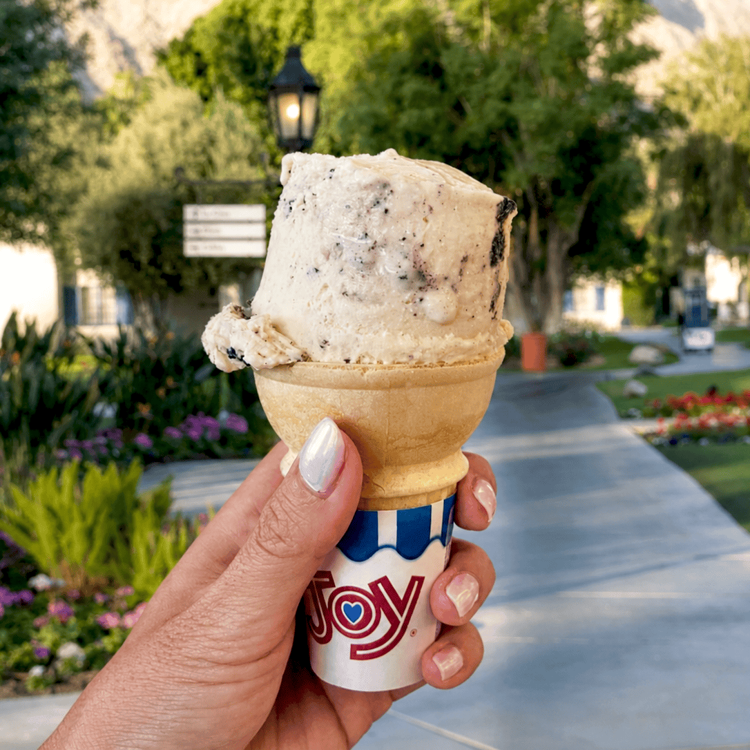 Hand holding ice cream cone at La Quinta Resort & Club in sunny garden.