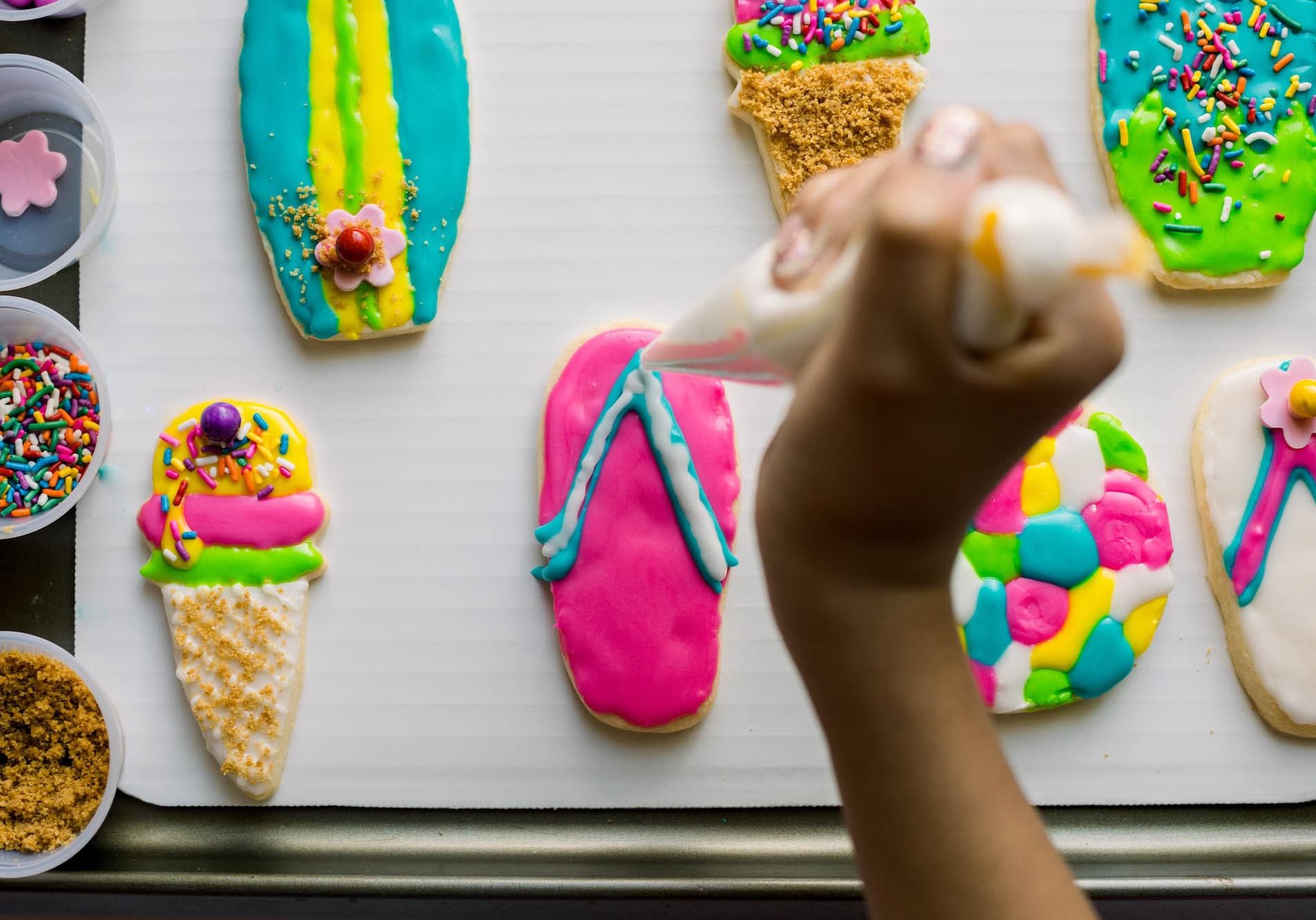 Hand decorating colorful Mother's Day cookies with icing and sprinkles.